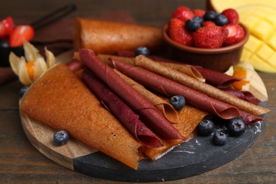 Photo of Delicious fruit leather rolls and berries on wooden table, closeup
