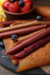 Photo of Delicious fruit leather rolls and berries on table, closeup