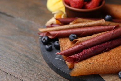 Photo of Delicious fruit leather rolls and berries on wooden table, closeup. Space for text