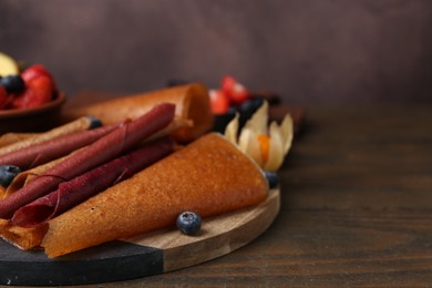Photo of Delicious fruit leather rolls and berries on wooden table, closeup. Space for text