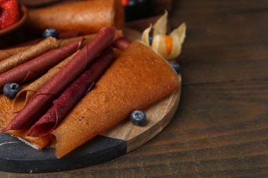 Photo of Delicious fruit leather rolls and berries on wooden table, closeup. Space for text