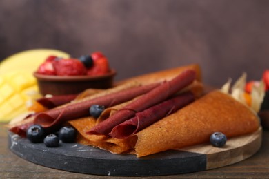 Photo of Delicious fruit leather rolls and berries on wooden table, closeup