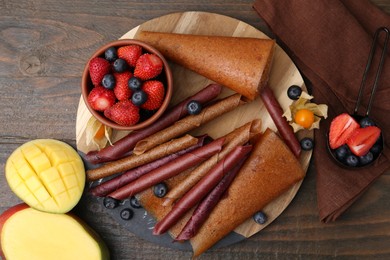 Photo of Delicious fruit leather rolls, mango and berries on wooden table, flat lay