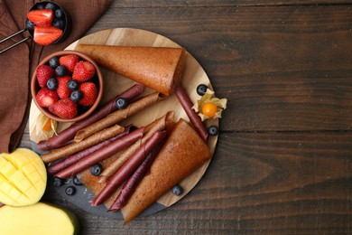 Photo of Delicious fruit leather rolls, mango and berries on wooden table, flat lay. Space for text