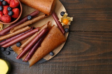 Photo of Delicious fruit leather rolls and berries on wooden table, flat lay. Space for text