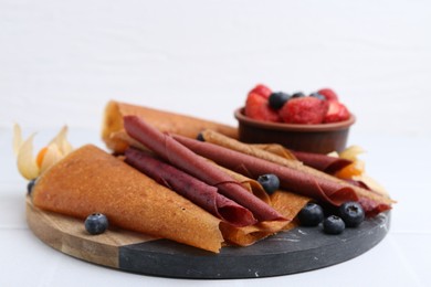 Photo of Delicious fruit leather rolls and berries on white table, closeup