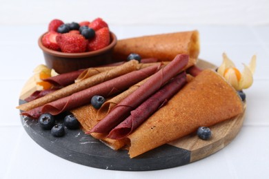 Photo of Delicious fruit leather rolls and berries on white table, closeup