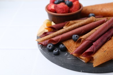Photo of Delicious fruit leather rolls and berries on white table, closeup. Space for text