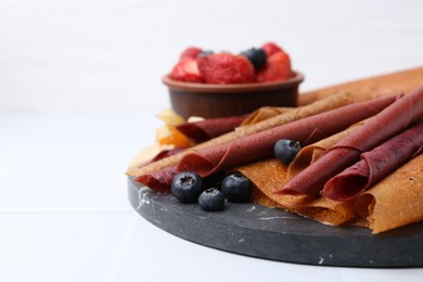Photo of Delicious fruit leather rolls and berries on white table, closeup. Space for text