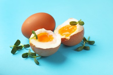 Photo of Soft boiled eggs with microgreens on light blue background, closeup