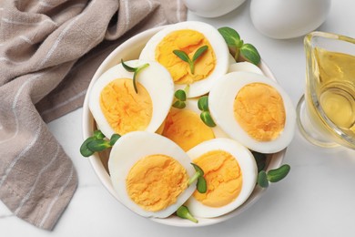 Photo of Halves of hard boiled eggs with microgreens on white table, flat lay