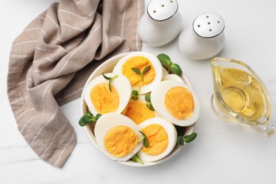 Photo of Halves of hard boiled eggs with microgreens on white table, flat lay
