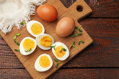 Photo of Halves of hard boiled eggs with microgreens on wooden table, top view