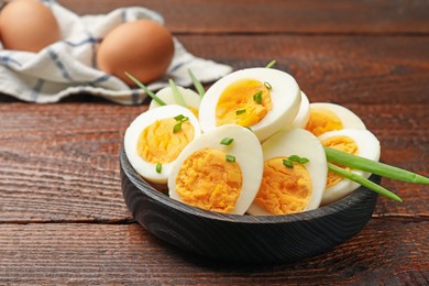 Photo of Halves of hard boiled eggs with green onions on wooden table, closeup