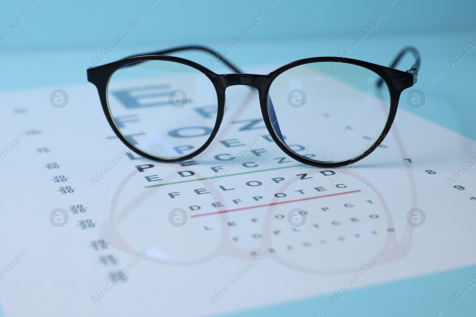 Glasses and vision test chart on light blue background, closeup Photo of Glasses and vision test chart on light blue background, closeup