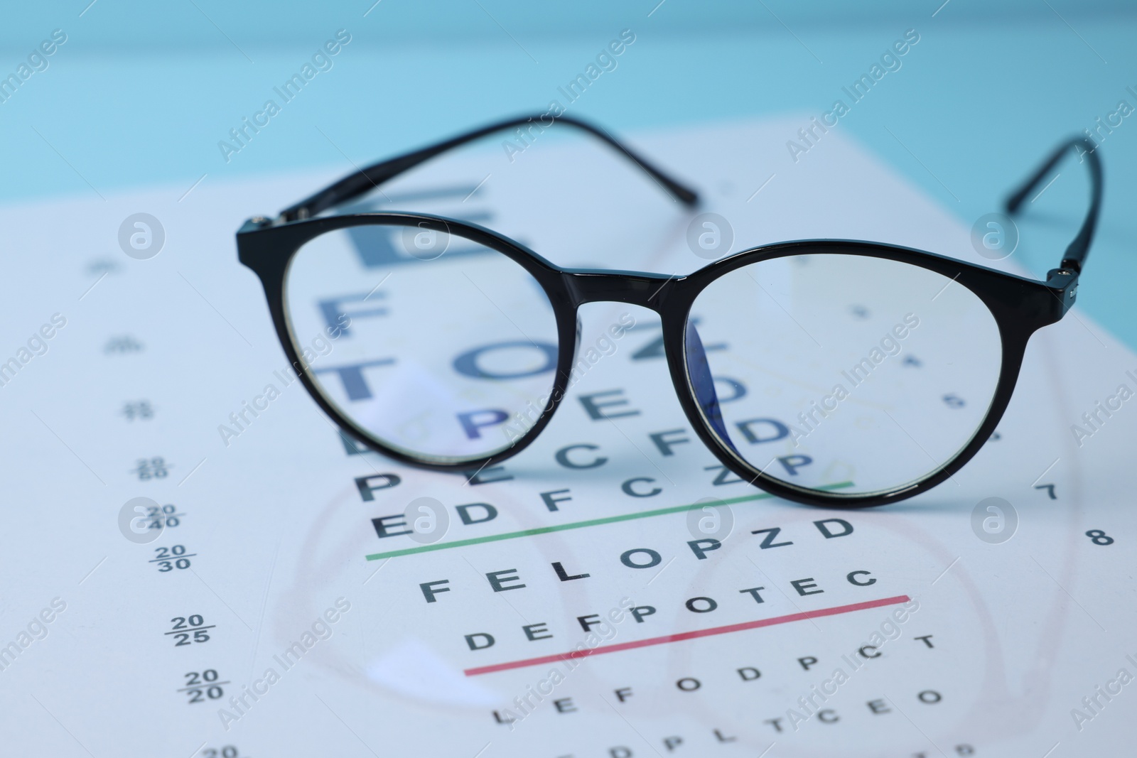 Glasses and vision test chart on light blue background, closeup Photo of Glasses and vision test chart on light blue background, closeup