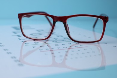 Photo of Glasses and vision test chart on light blue background, closeup