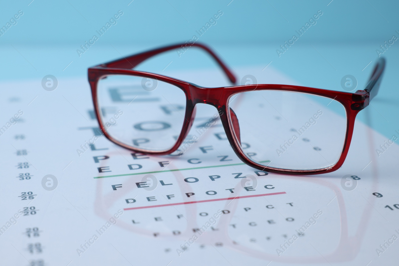 Glasses and vision test chart on light blue background, closeup Photo of Glasses and vision test chart on light blue background, closeup