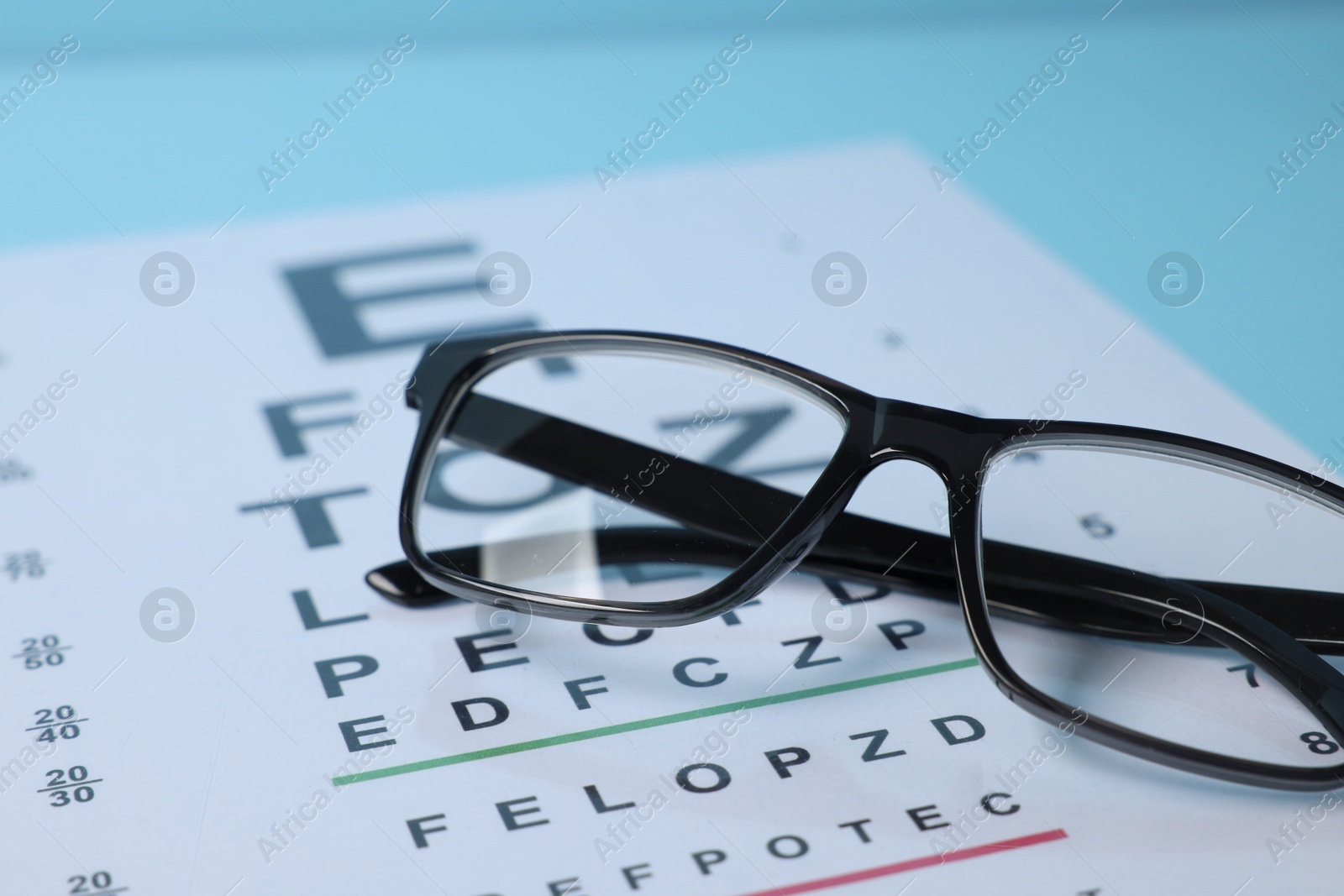 Glasses and vision test chart on light blue background, closeup Photo of Glasses and vision test chart on light blue background, closeup