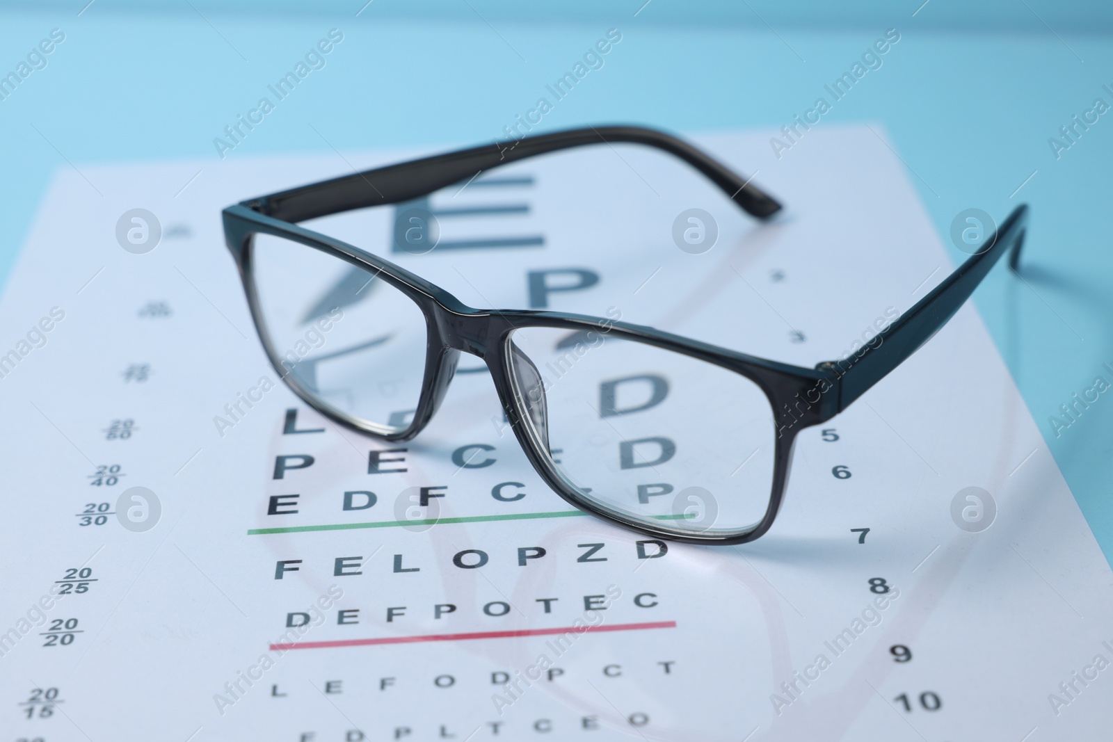 Glasses and vision test chart on light blue background, closeup Photo of Glasses and vision test chart on light blue background, closeup