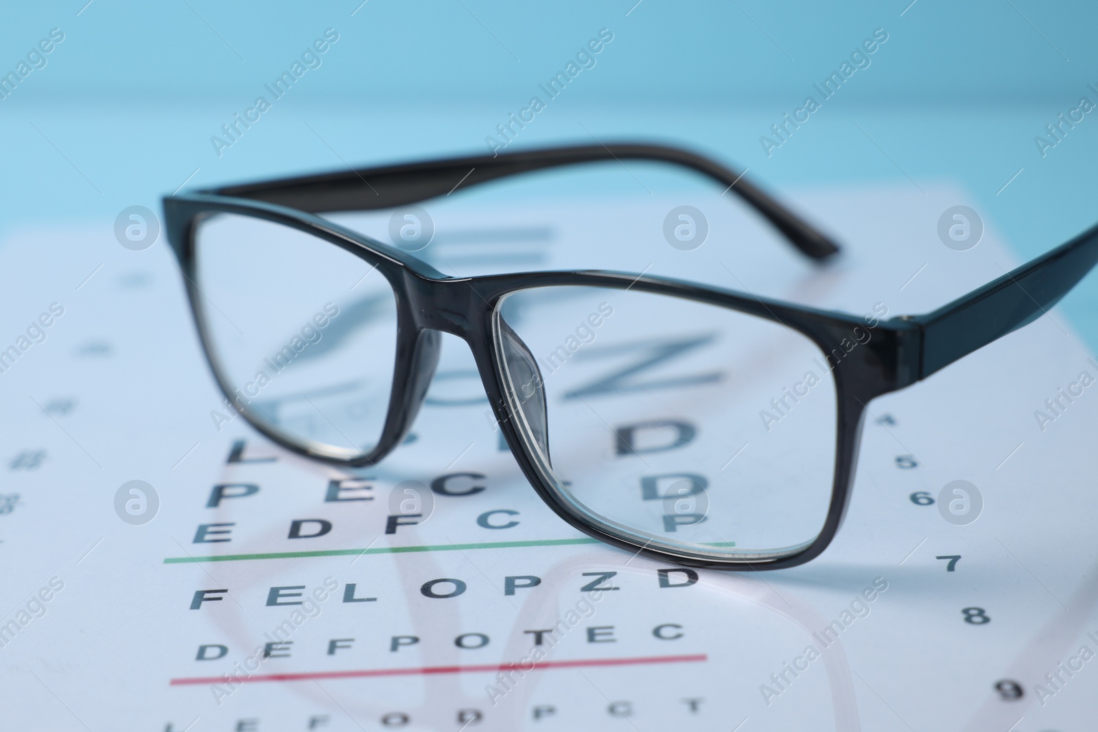 Glasses and vision test chart on light blue background, closeup Photo of Glasses and vision test chart on light blue background, closeup