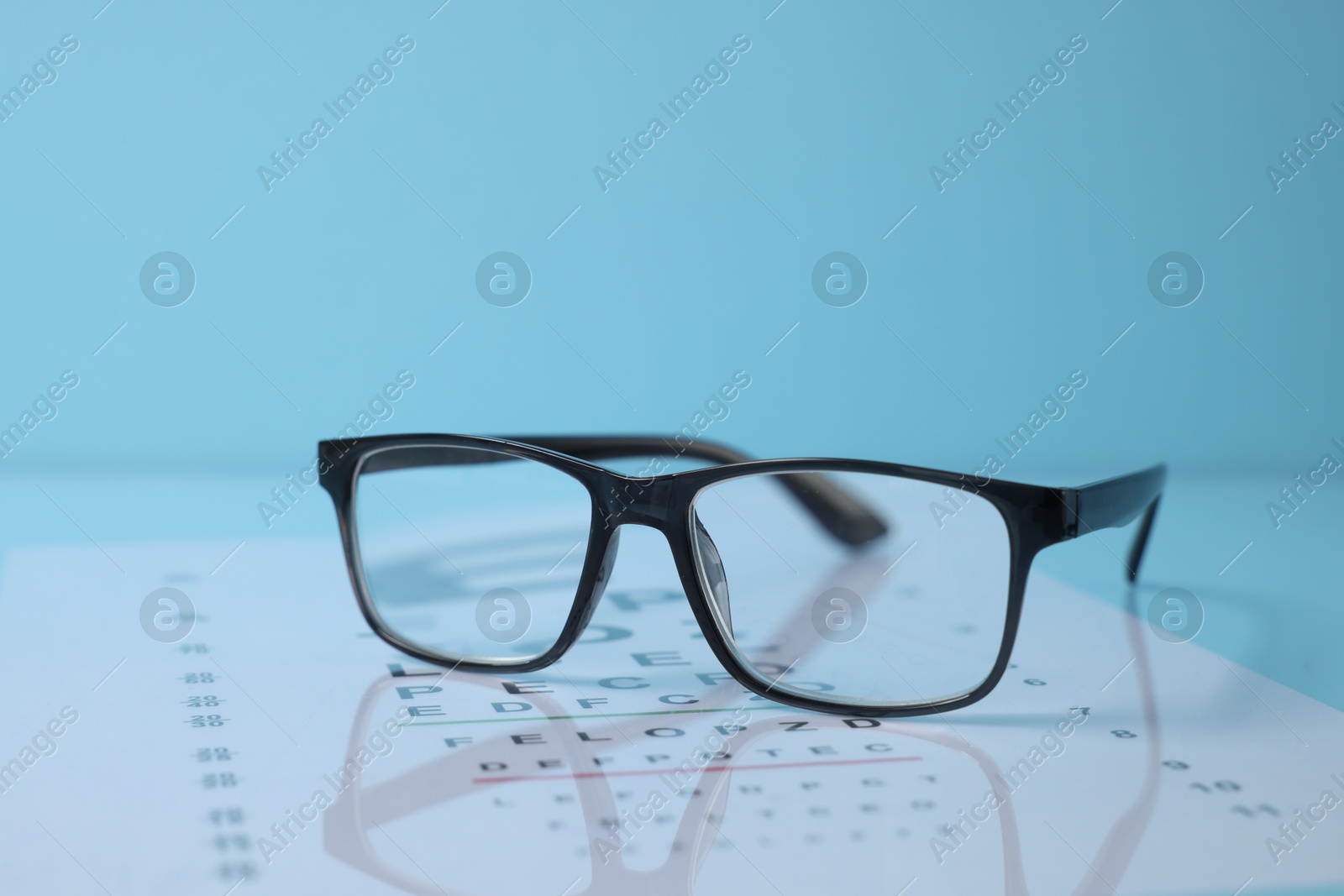 Glasses and vision test chart on light blue background, closeup Photo of Glasses and vision test chart on light blue background, closeup