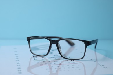 Photo of Glasses and vision test chart on light blue background, closeup