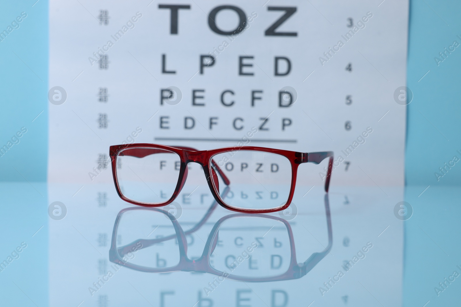 Glasses on light blue table against vision test chart, closeup Photo of Glasses on light blue table against vision test chart, closeup