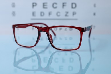 Photo of Glasses on light blue table against vision test chart, closeup