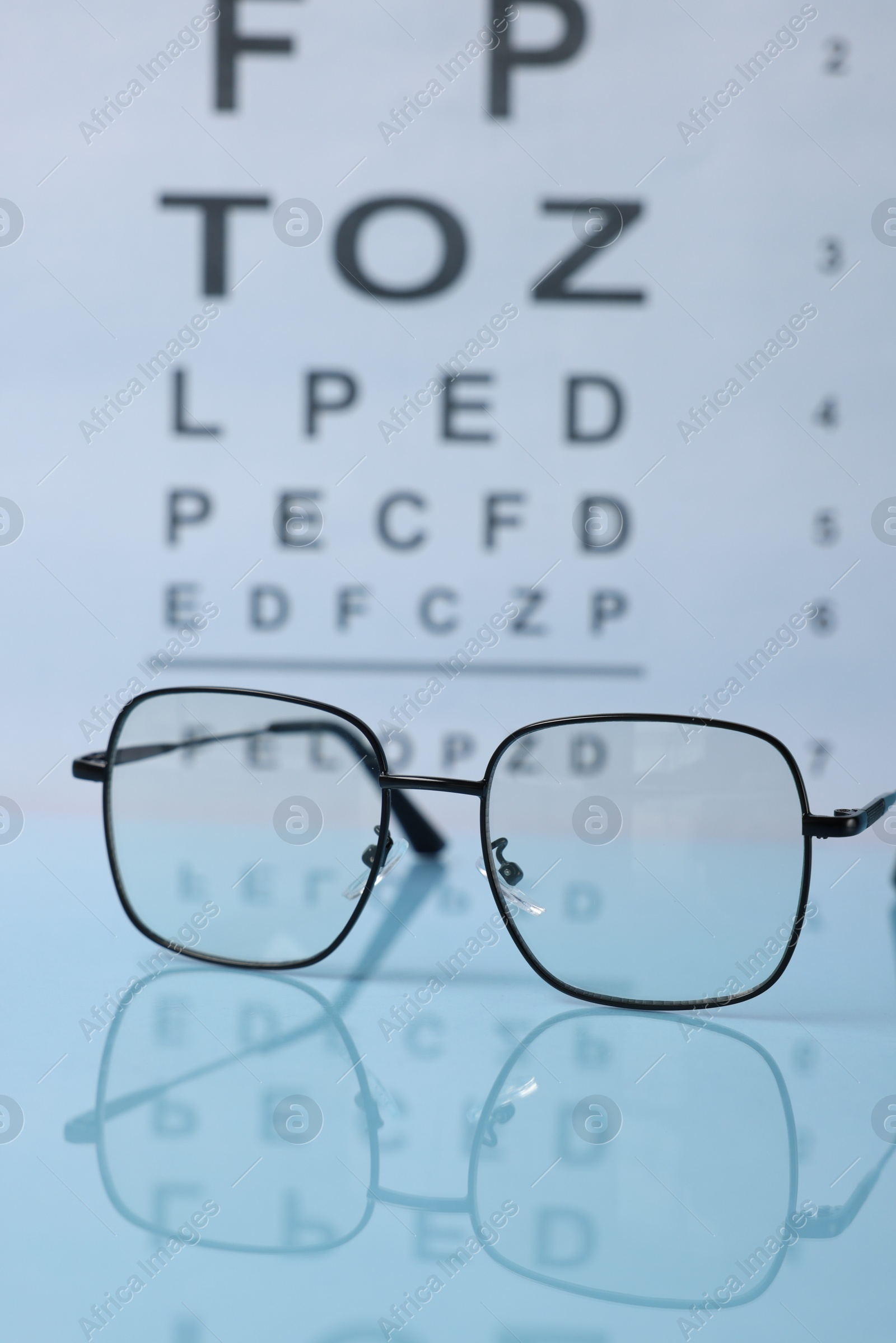 Glasses on light blue table against vision test chart, closeup Photo of Glasses on light blue table against vision test chart, closeup