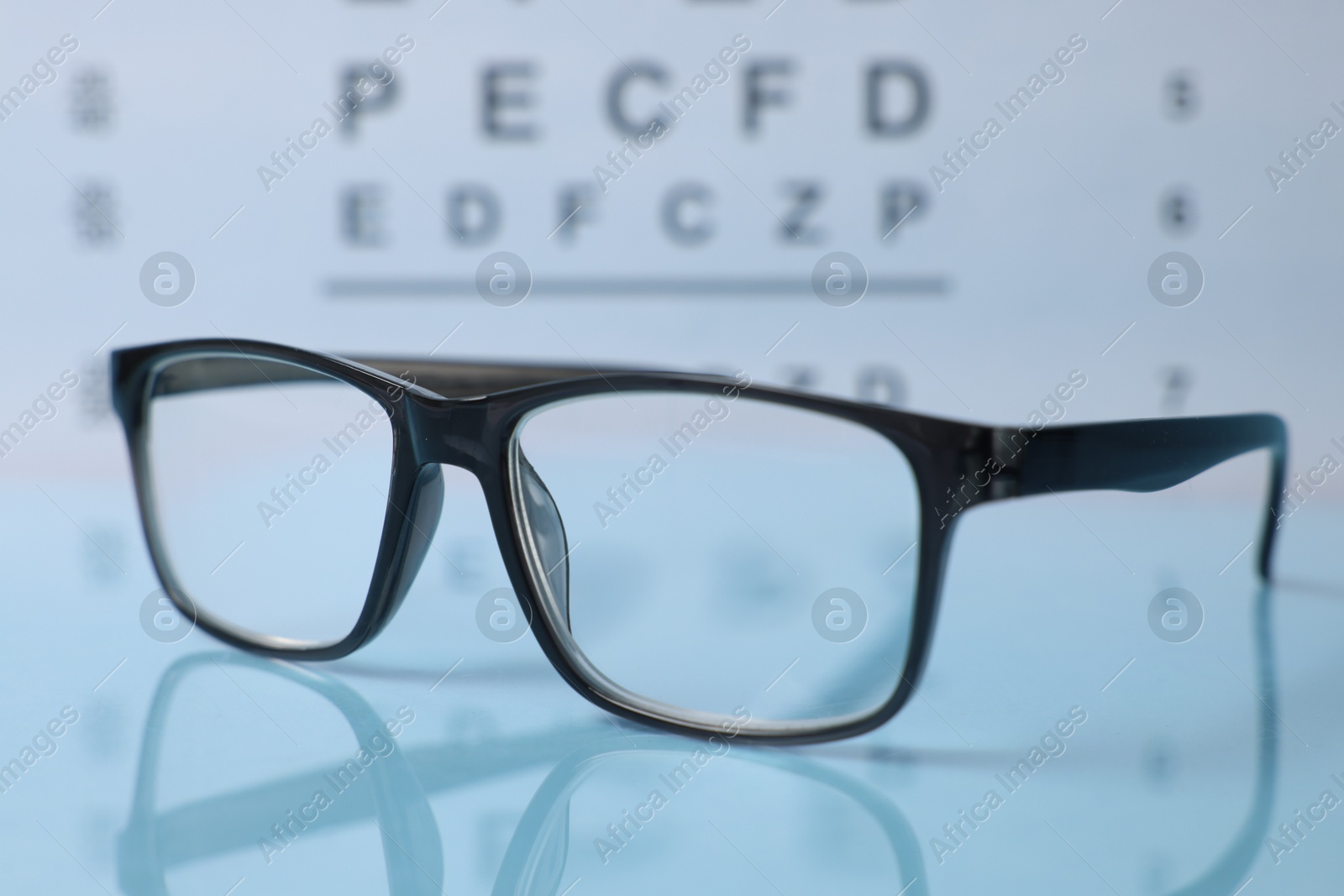 Glasses on light blue table against vision test chart, closeup Photo of Glasses on light blue table against vision test chart, closeup