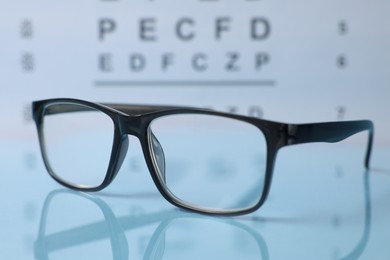 Photo of Glasses on light blue table against vision test chart, closeup