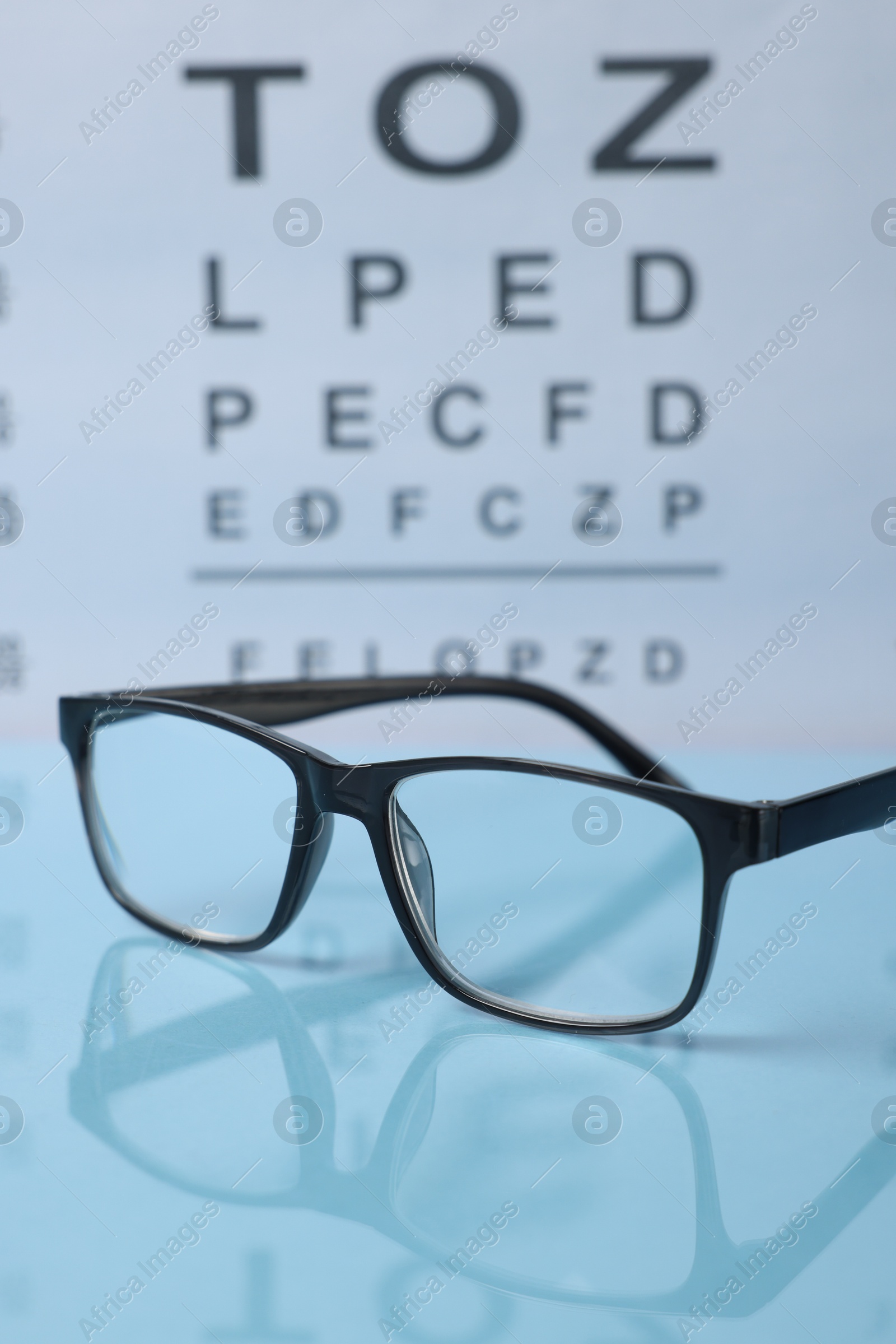 Glasses on light blue table against vision test chart, closeup Photo of Glasses on light blue table against vision test chart, closeup
