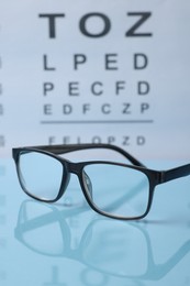 Photo of Glasses on light blue table against vision test chart, closeup