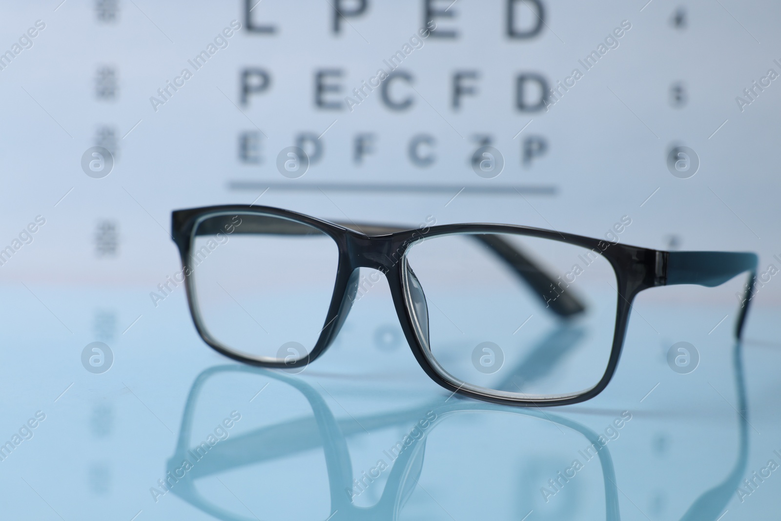 Glasses on light blue table against vision test chart, closeup Photo of Glasses on light blue table against vision test chart, closeup