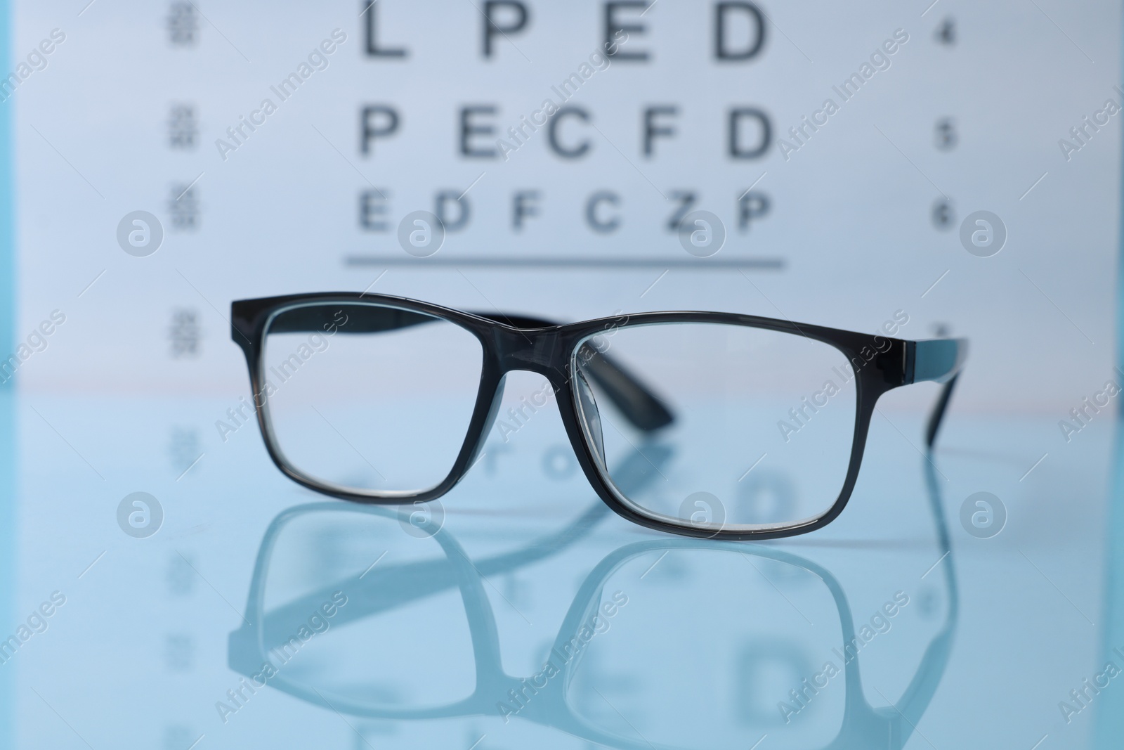 Glasses on light blue table against vision test chart, closeup Photo of Glasses on light blue table against vision test chart, closeup