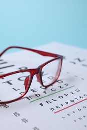 Photo of Glasses and vision test chart on light blue background, closeup