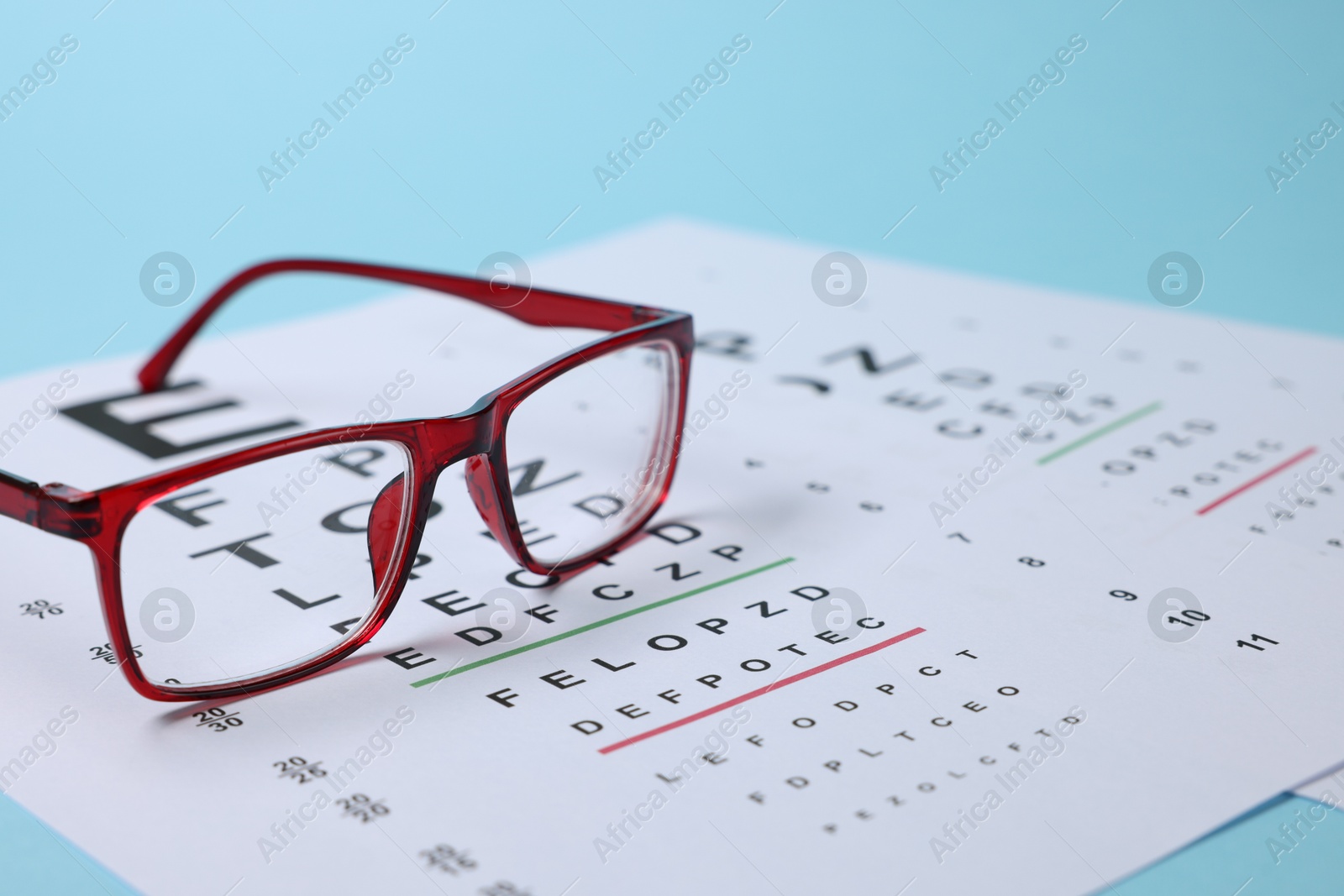 Glasses and vision test chart on light blue background, closeup Photo of Glasses and vision test chart on light blue background, closeup