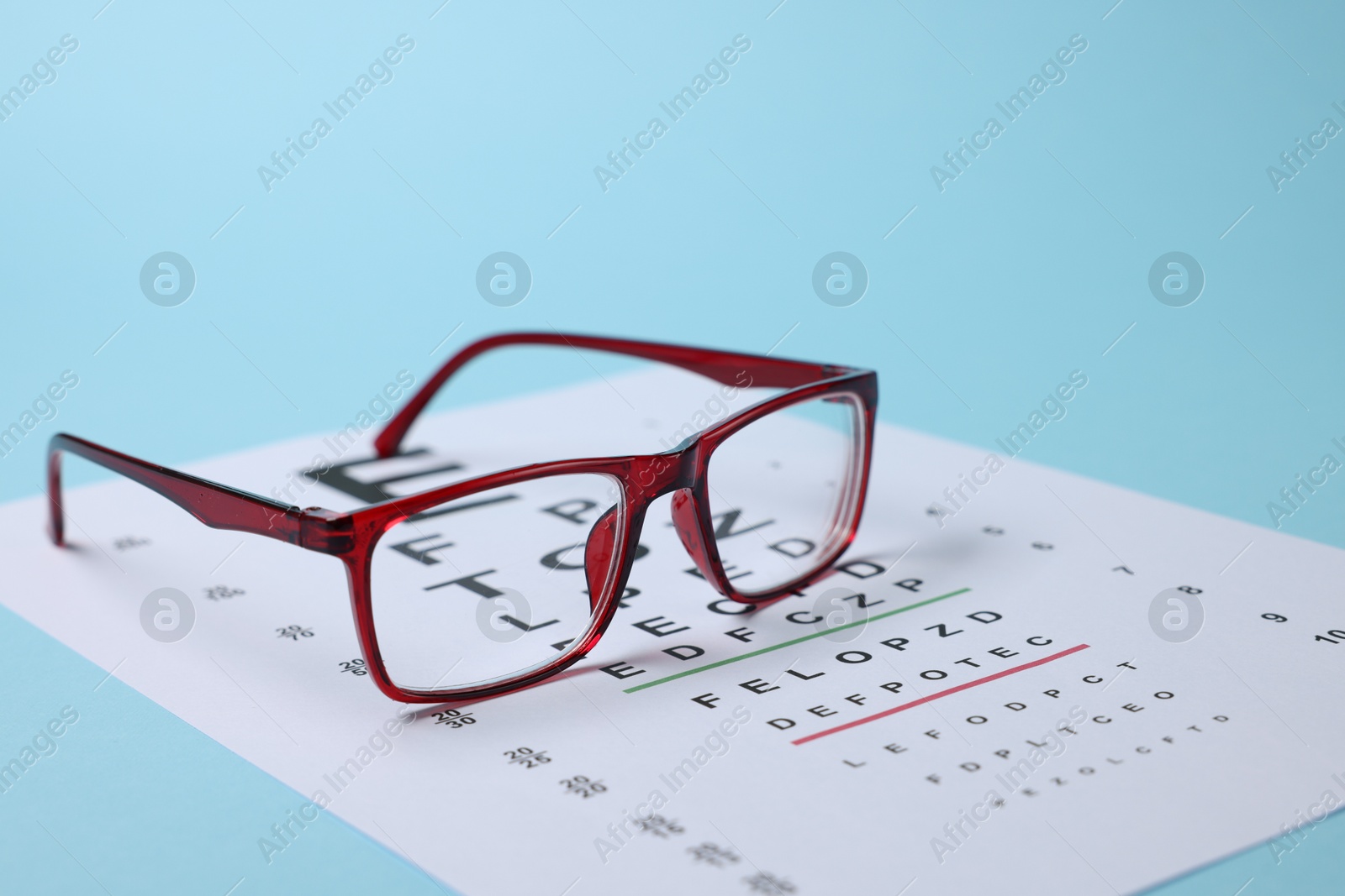 Glasses and vision test chart on light blue background, closeup Photo of Glasses and vision test chart on light blue background, closeup