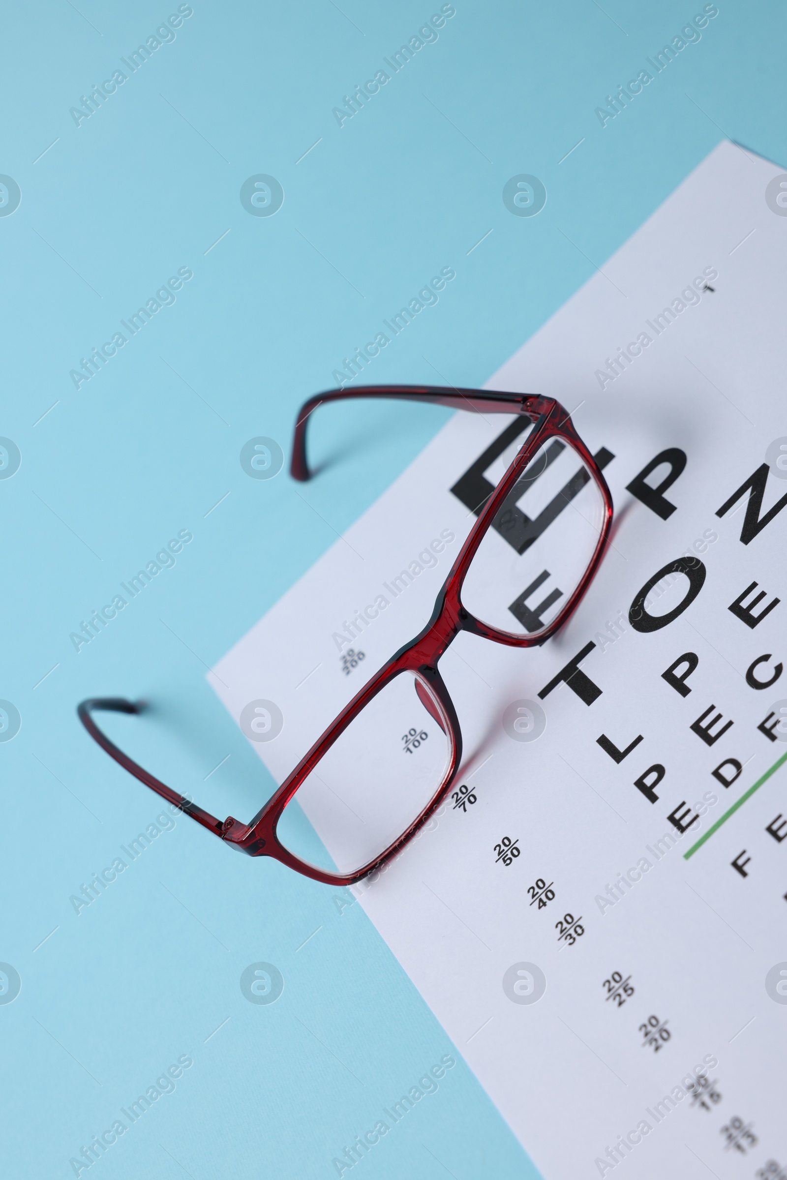 Glasses and vision test chart on light blue background, closeup Photo of Glasses and vision test chart on light blue background, closeup