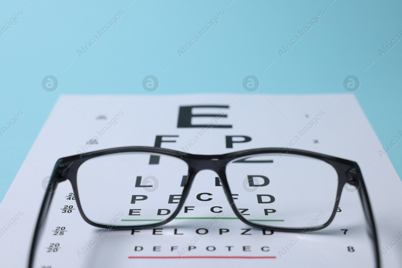 Glasses and vision test chart on light blue background, closeup Photo of Glasses and vision test chart on light blue background, closeup