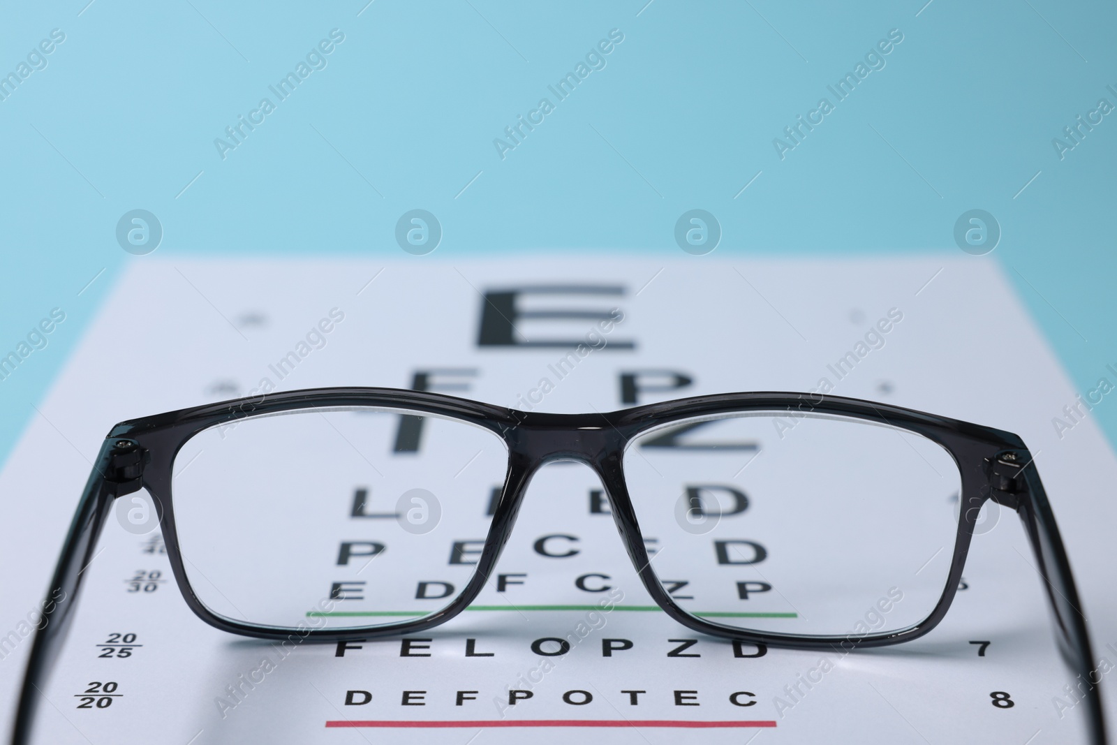 Glasses and vision test chart on light blue background, closeup Photo of Glasses and vision test chart on light blue background, closeup