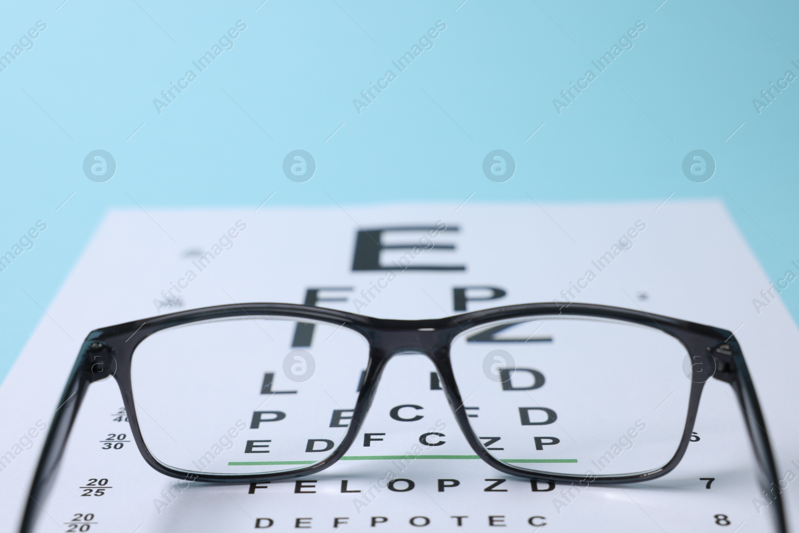 Glasses and vision test chart on light blue background, closeup Photo of Glasses and vision test chart on light blue background, closeup