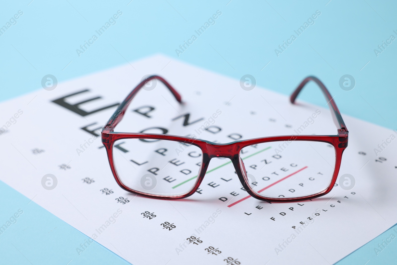 Glasses and vision test chart on light blue background, closeup Photo of Glasses and vision test chart on light blue background, closeup