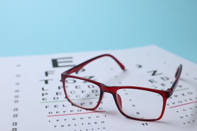 Photo of Glasses and vision test chart on light blue background, closeup