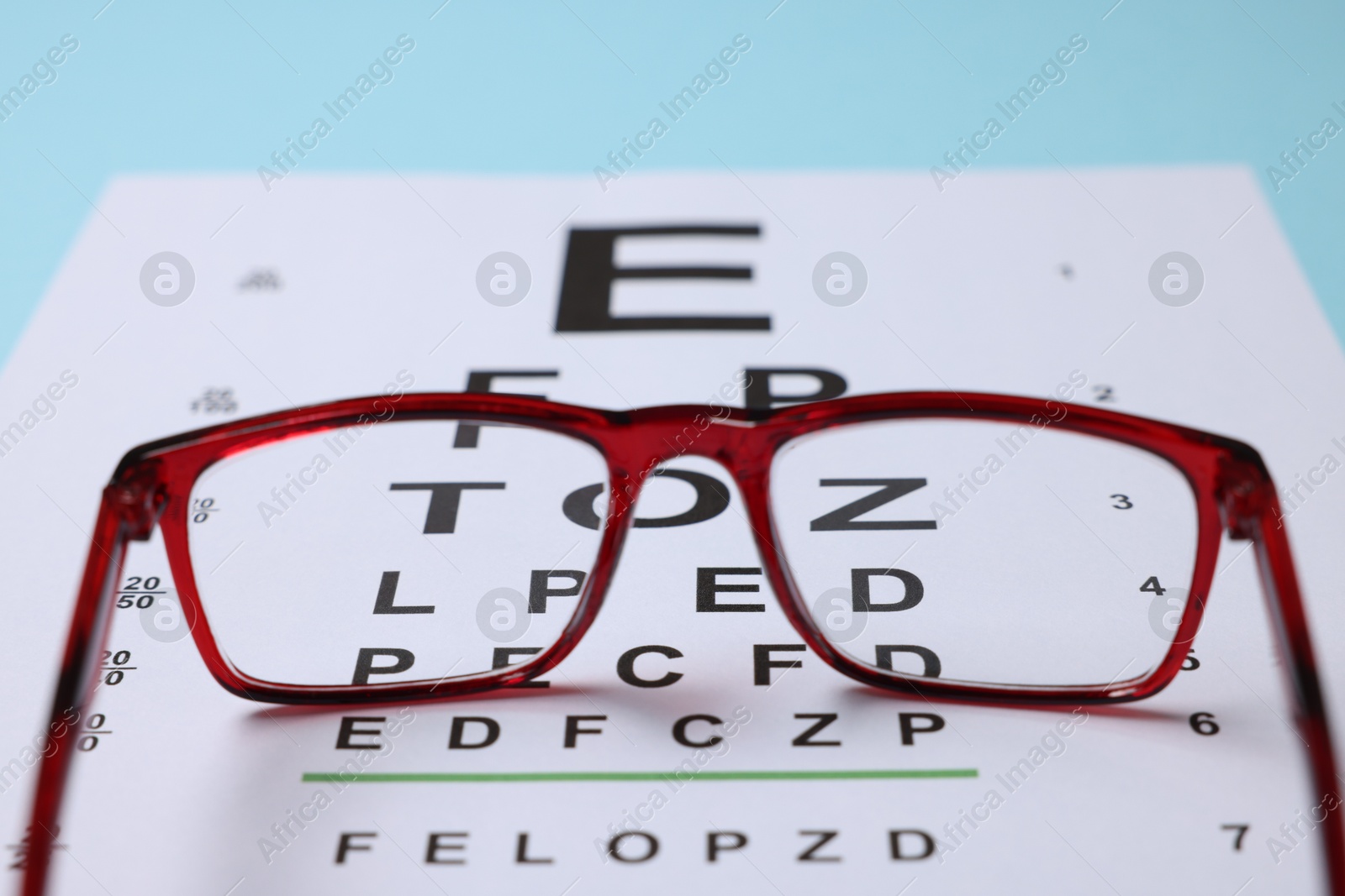 Glasses and vision test chart on light blue background, closeup Photo of Glasses and vision test chart on light blue background, closeup
