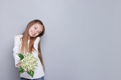 Photo of Girl with bouquet of beautiful lily-of-the-valley flowers on light grey background. Space for text