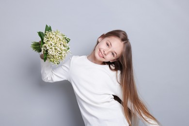 Photo of Girl with bouquet of beautiful lily-of-the-valley flowers on light grey background