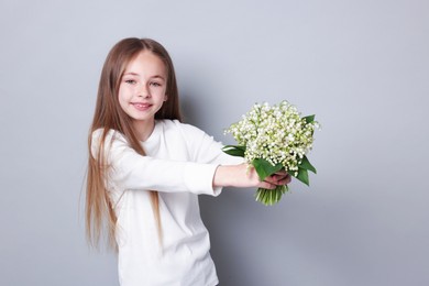 Photo of Girl with bouquet of beautiful lily-of-the-valley flowers on light grey background