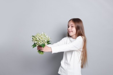 Photo of Girl with bouquet of beautiful lily-of-the-valley flowers on light grey background